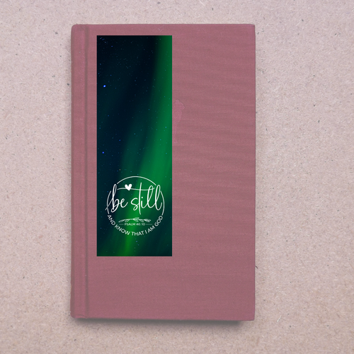 Pink notebook with a green screen displaying 'Be still' text on a textured beige background