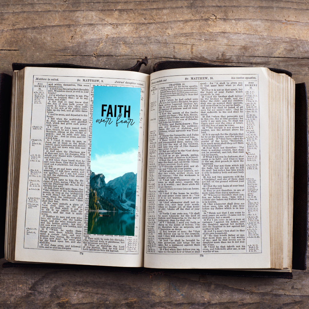 Open book with a blue bookmark featuring 'Faith over Fear' on a wooden surface