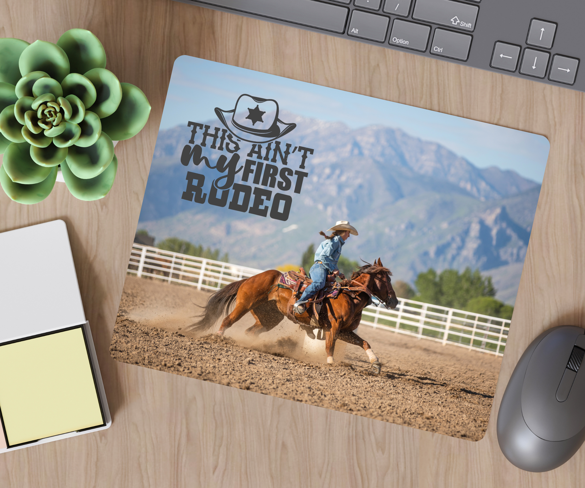 Mouse pad with a cowboy riding a horse design on a desk with a keyboard and plant.
